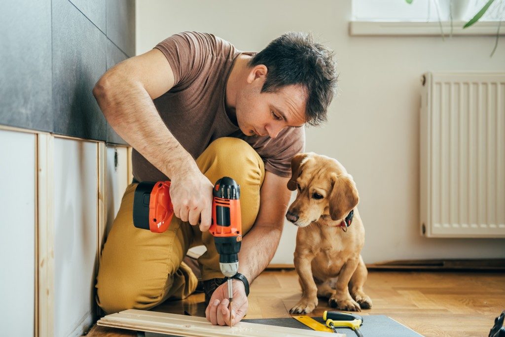 man drilling a plank of wood beside his dog