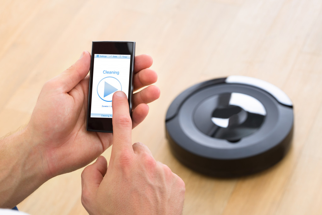 A man holding a phone and pressing the button to start a robot vacuum